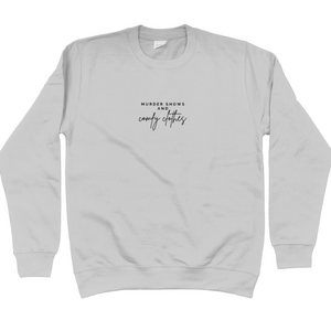 Heather Grey Sweatshirt that says: Murder shows and comfy clothes. Murder shows is in caps and sans serif style font, comfy clothes is in a handwritten style font. Text is small and placed in the centre of the chest, stretching as far as the neckline