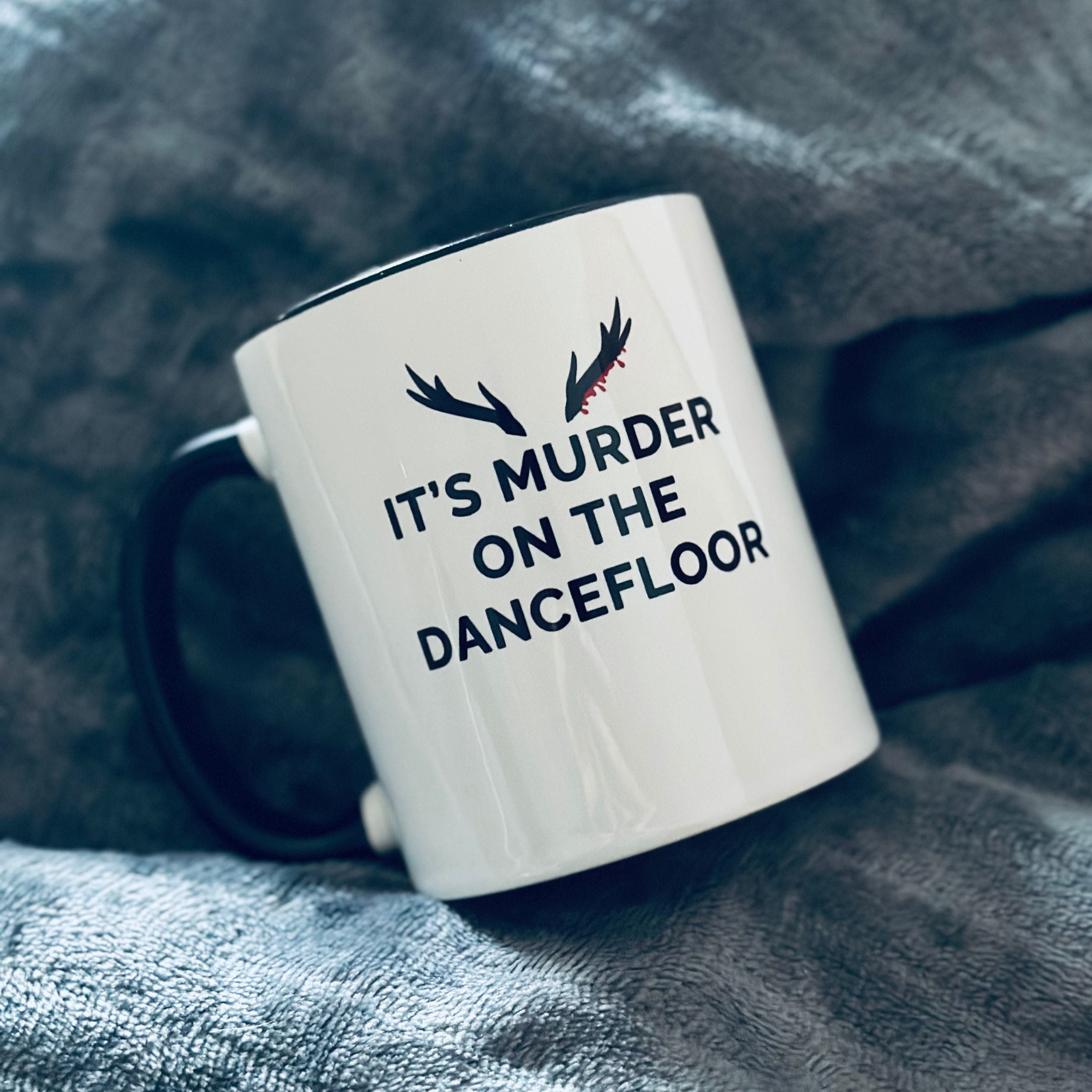 Mug with a black handle and black inner that reads "It's Murder On The Dancefloor" with antlers above the text with blood drips coming from the right bottom antler