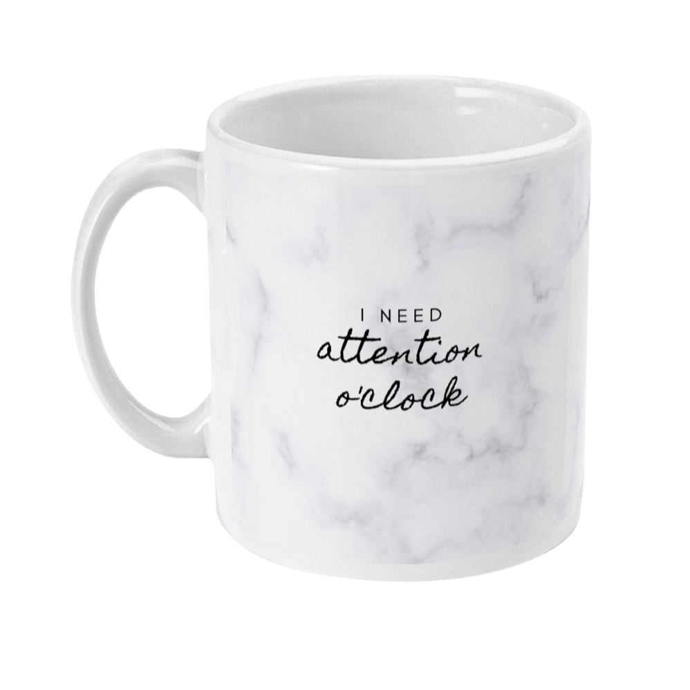 Mug with a light marble print that says: I need attention o'clock