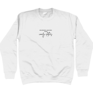 Arctic White Sweatshirt that says: Murder shows and comfy clothes. Murder shows is in caps and sans serif style font, comfy clothes is in a handwritten style font. Text is small and placed in the centre of the chest, stretching as far as the neckline