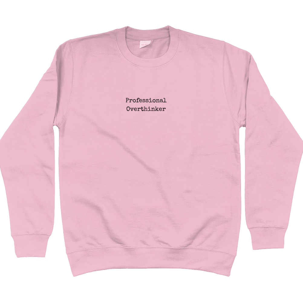 Sweatshirt in baby pink with black text in typewriter font that says: Professional Overthinker. Text is in the middle of the chest and small in size