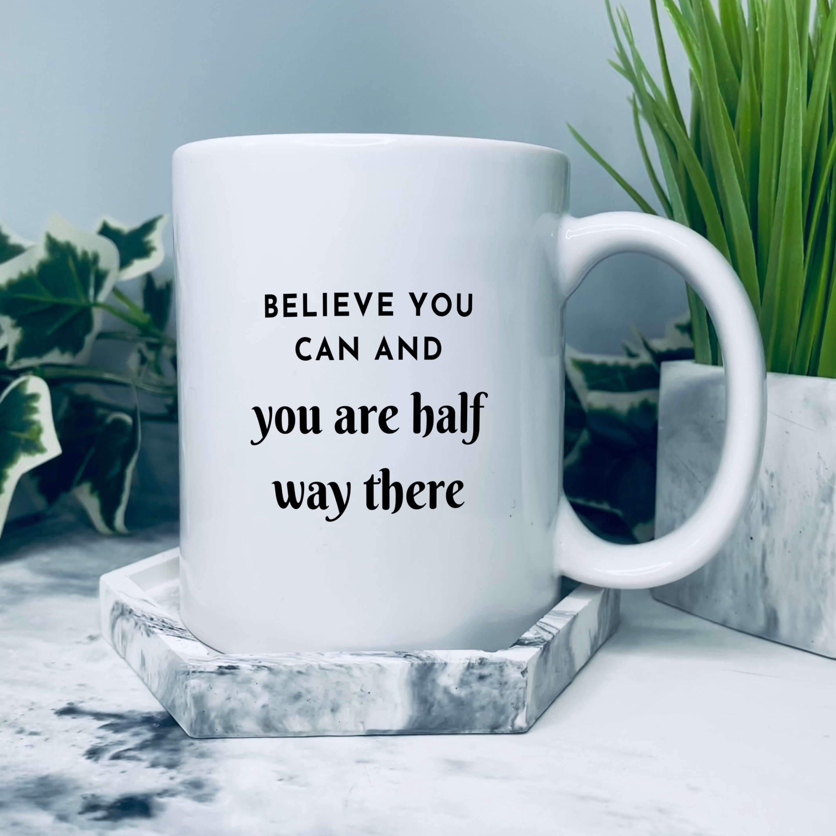 Mug in a setting on a grey marbled coaster. Mug reads: believe you can and you are half way there