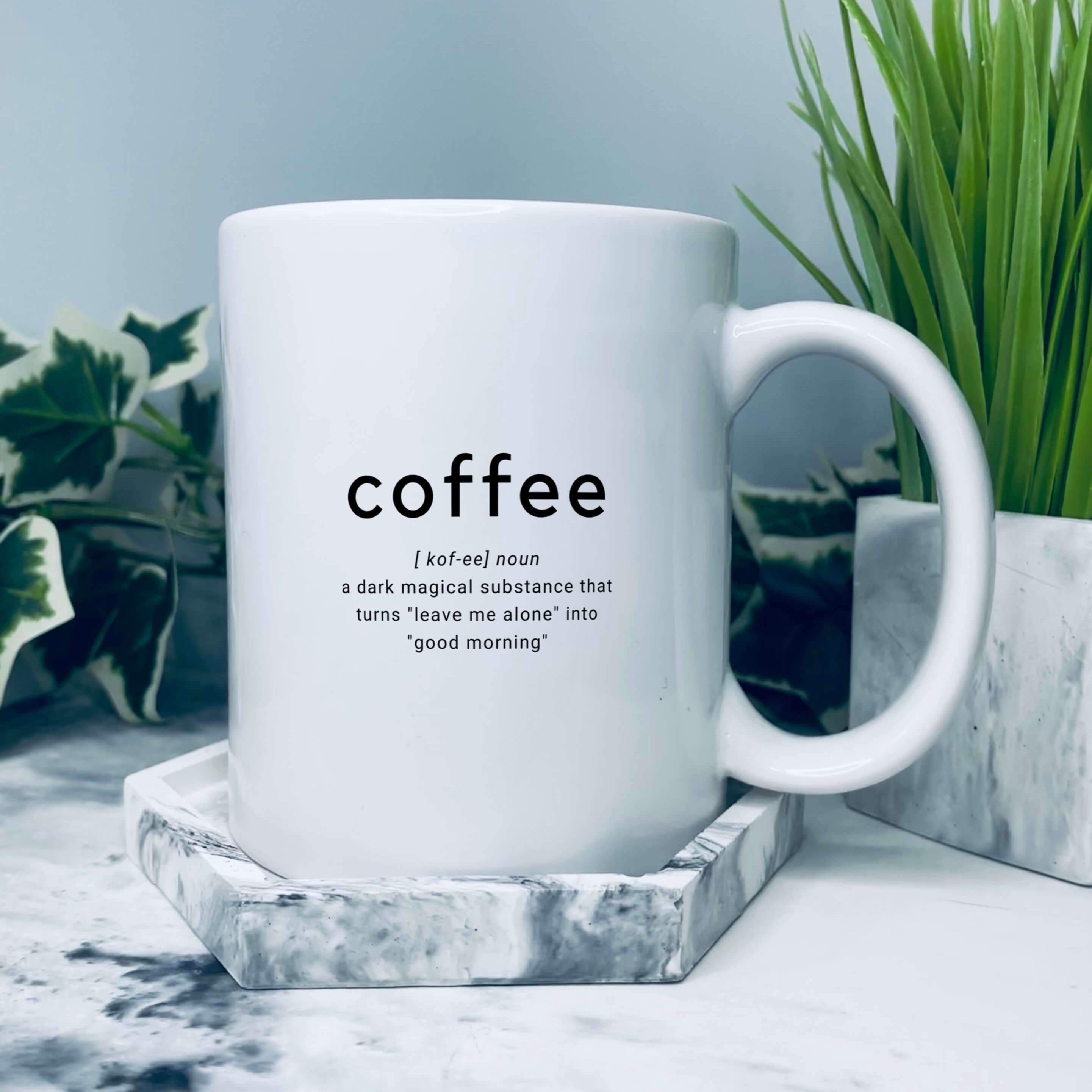 Coffee mug. Mug has coffee in larger text, with text underneath that says: a dark magical substance that turns leave me alone into good morning