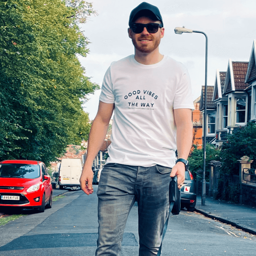 Arctic white organic t-shirt that reads good vibes all the way. The positive affirmation club. Good vibes all the way is in larger text with good vibes arched over the text that then reads all the way. The positive affirmation club text is in a small text that sits underneath good vibes all the way.