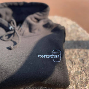 Jet Black hoodie that reads positivitea on the left hand side of the hoodie in a logo sized style. The tea section of the word has a takeaway style cup around it to give a spin on the positivitea word