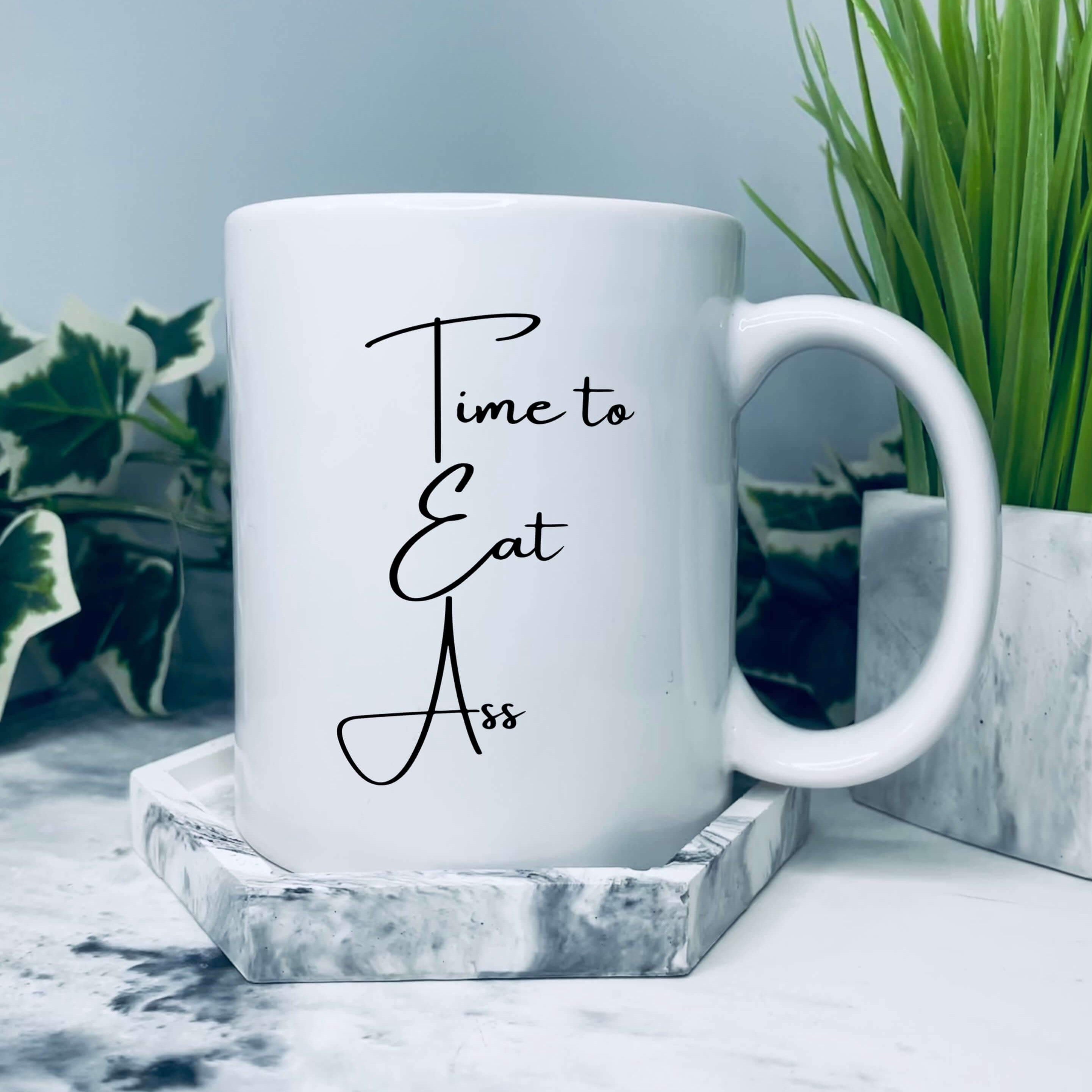 Mug that says: Time to Eat Ass. The T,E and A are capitalised and positioned above one another so the mug also reads tea.