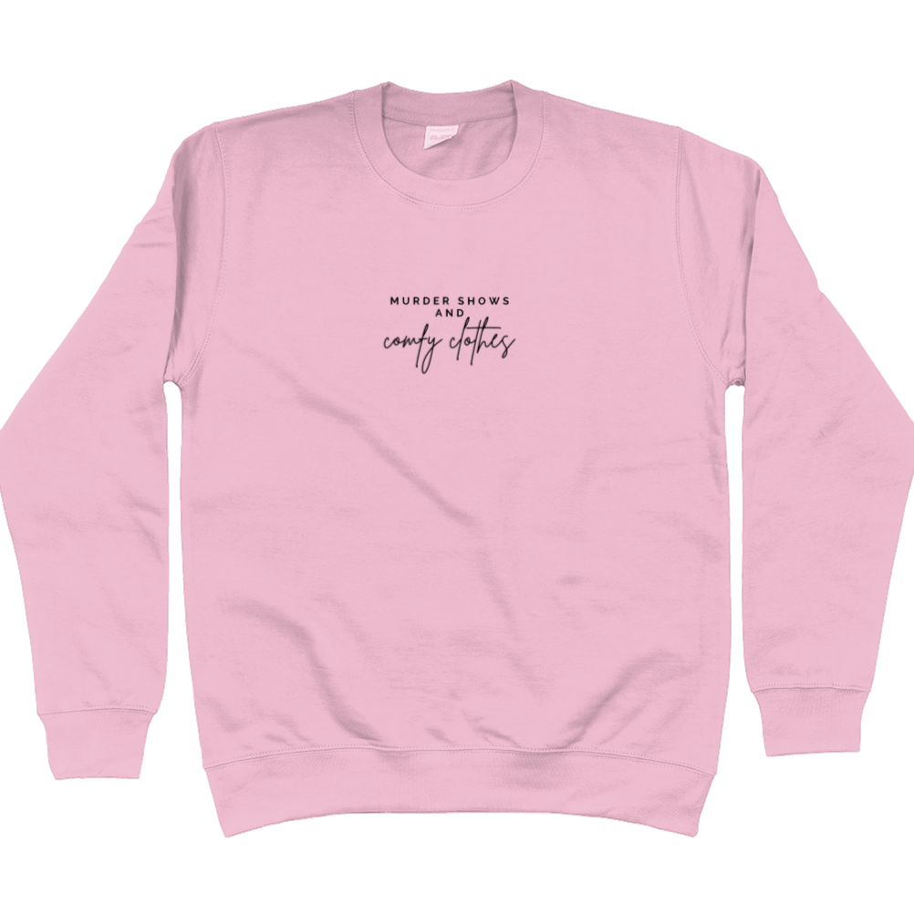 Baby Pink Sweatshirt that says: Murder shows and comfy clothes. Murder shows is in caps and sans serif style font, comfy clothes is in a handwritten style font. Text is small and placed in the centre of the chest, stretching as far as the neckline